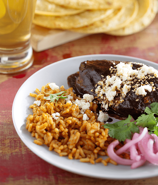 Chicken with Mole Negro served on a white plate with a beverage