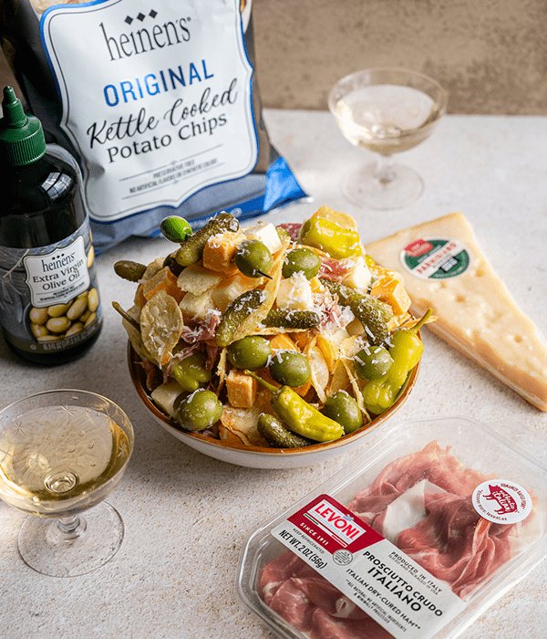 the Italian Kettle Chip Snack Bowl plated in a white bowl on a table. Surrounded by olive oil, kettle chips, & cheese
