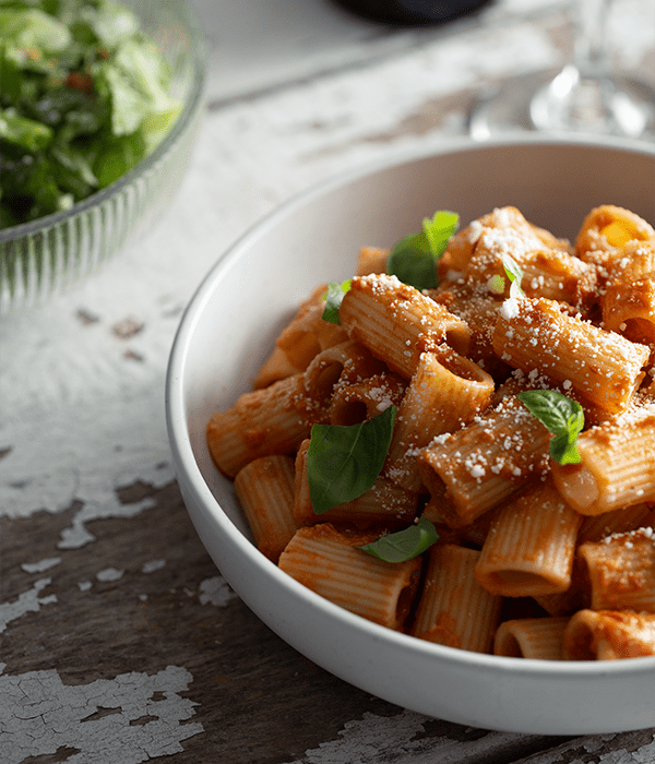Mezzi Rigatoni ala Vodka in a white bowl served with a side salad