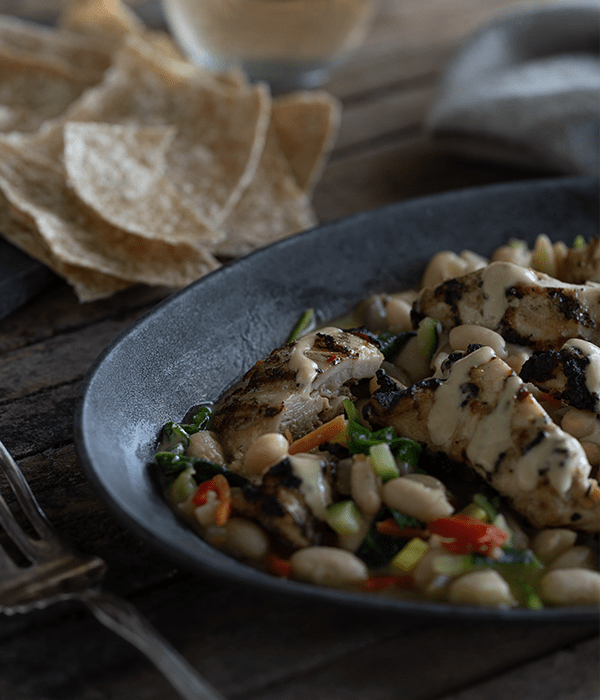 SoCo Tahini and Date Chicken with Beans and Vegetables served in a black bowl with some tortilla chips