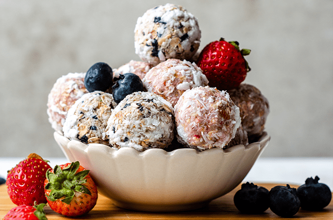 Strawberry & Blueberry Energy Bites in a white bowl surrounded by some other berries