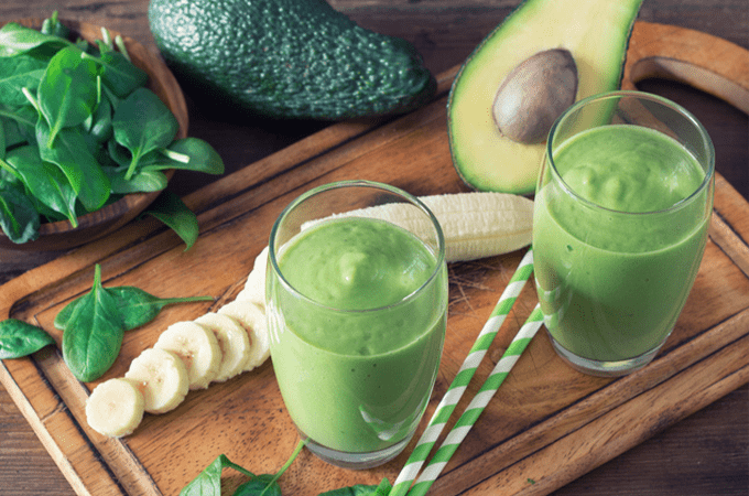 2 Super Energizing Smoothies on a cutting board next to some avocadoes and bananas