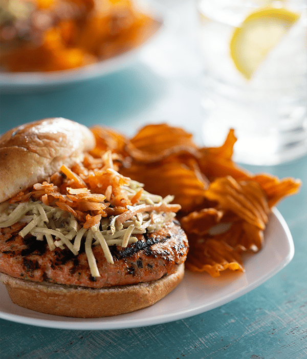 Tropical Salmon Burger with Asian Slaw served on a white plate with veggie chips