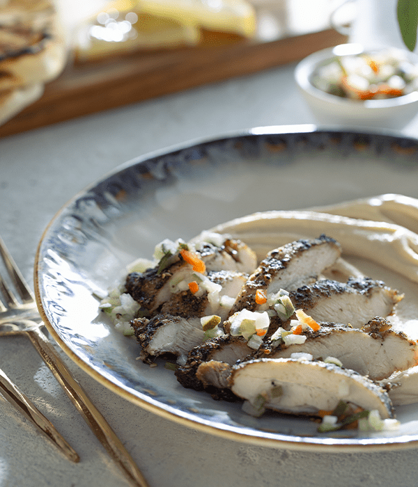ZATAR MARINATED CHICKEN HUMMUS BOWL served on a plate with some utensils and lemon slices
