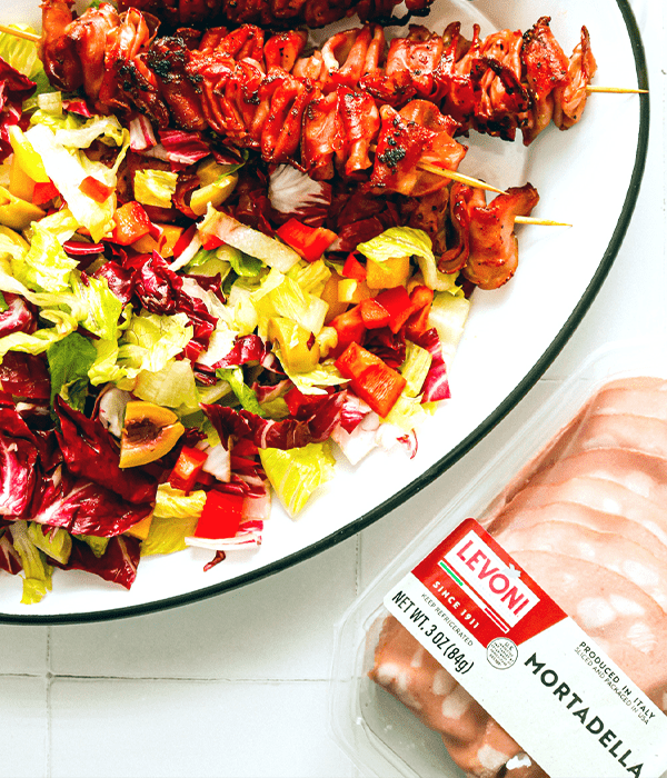 the Crispy Mortadella Skewers being served on a white plate next to some packaged Levoni Mortadella