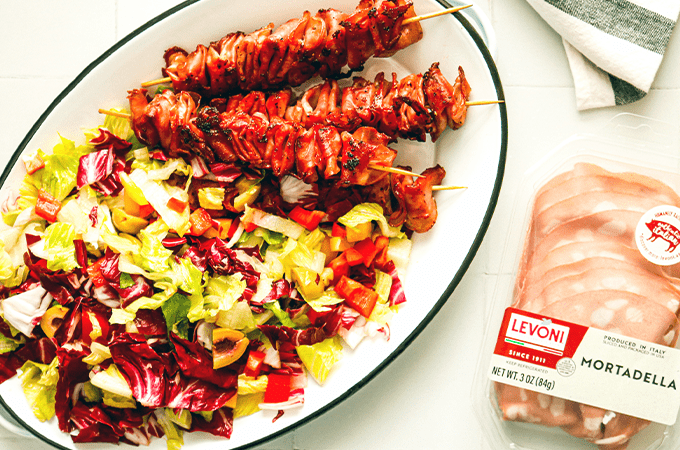 the Crispy Mortadella Skewers being served on a white plate next to some packaged Levoni Mortadella