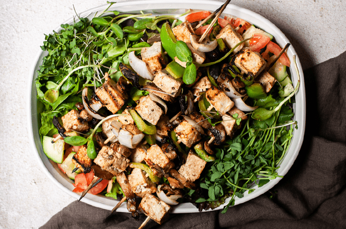 Grilled Tofu and Mushroom Skewers on a white plate on a grey table