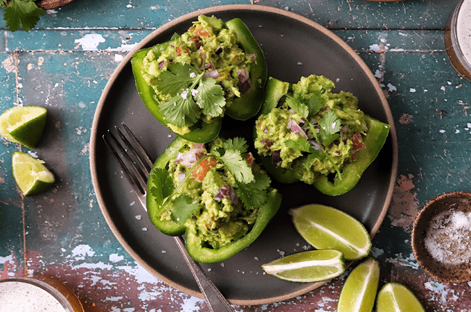 Plant-Powered Guacamole Stuffed Peppers served on a brown plate with some lime slices