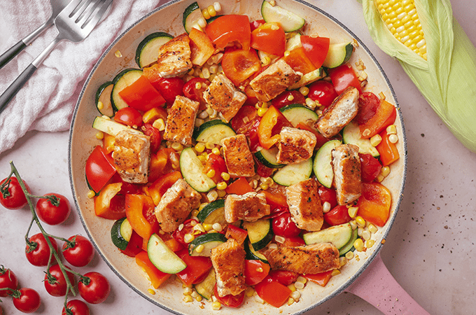 Summer Vegetable Skillet with Salmon Bites served in a pan with a side of corn and tomatoes