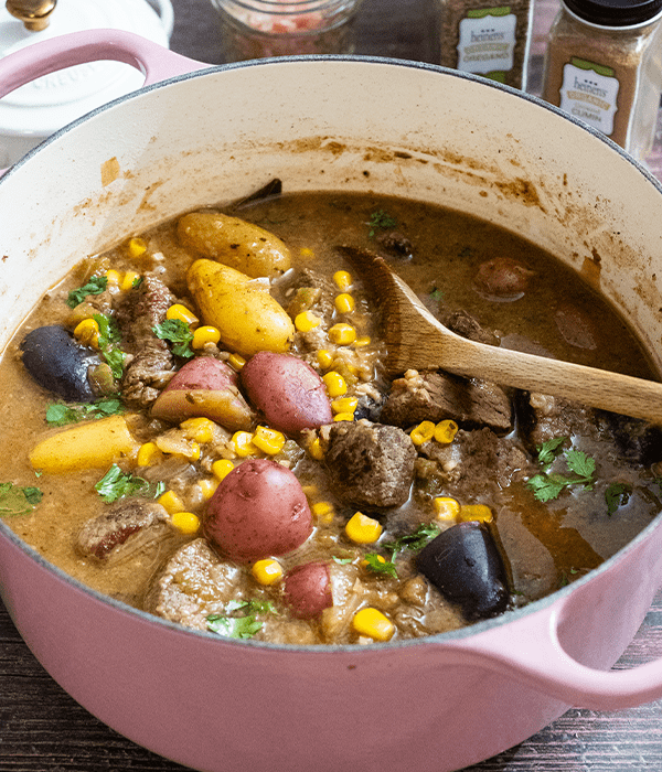 Hatch Chile Beef Stew sitting in a pink pot being stirred with a wooden spoon