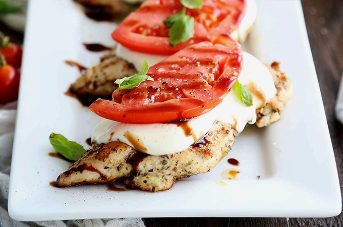 Grilled chicken caprese plated with mozzarella, tomato, and balsamic glaze