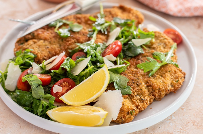 Chicken Milanese plated with salad and a lemon wedge