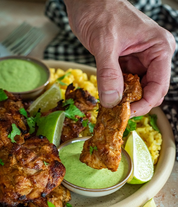 A hand dipping a peruvian chicken thigh into aji verde sauce