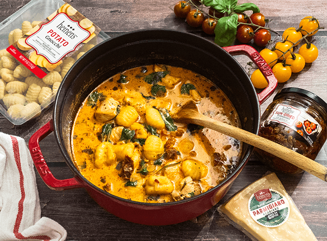 Marry Me Chicken Gnocchi Soup finished in a pot surrounded by its ingredients on a wooden table