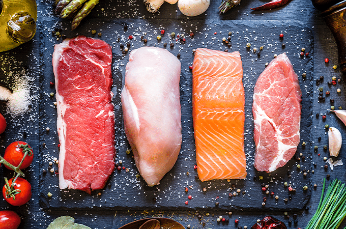 raw steak, chicken, salmon, and pork on a black table