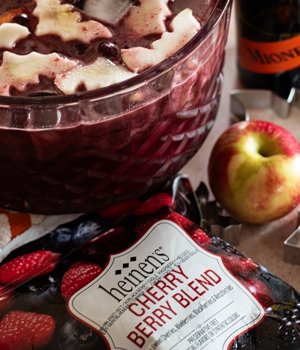 A bowl of Halloween punch with bat-shaped apples surrounded by Heinen's frozen Cherry Berry Blend fruit and an apple.