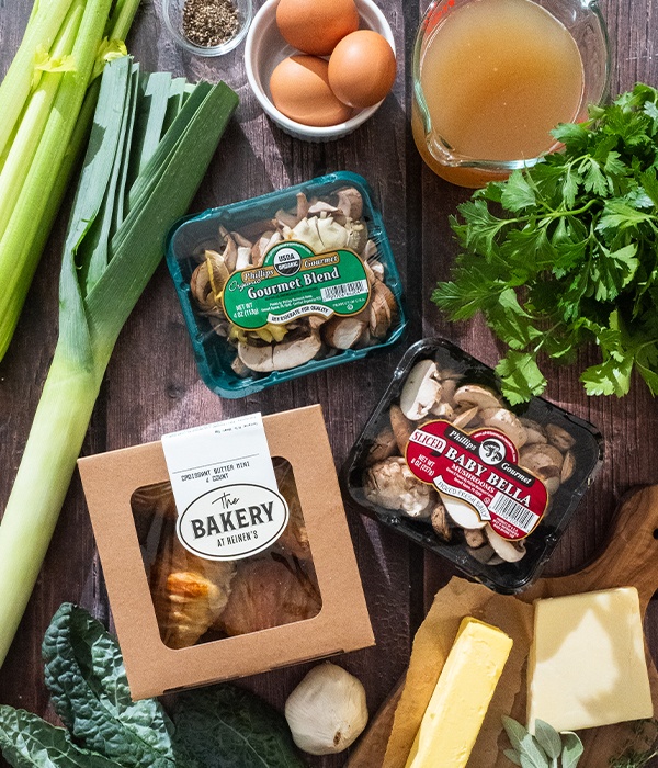 Ingredients for Mushroom Croissant Stuffing on a table, including croissants, mushrooms, butter, stock, eggs, cheese and assorted vegetables