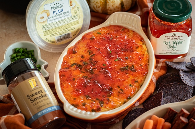 A baked dish of pepper jelly cream cheese dip surrounded by cream cheese spread, red pepper jelly, and sweet & smokey seasoning.
