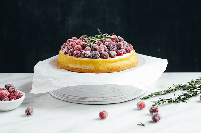 Cheesecake topped with sugared cranberries and rosemary garnish