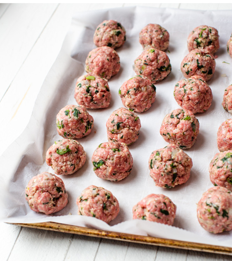 Rolled meatballs on parchment paper covered pan