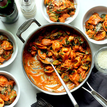 Spinach and tomato torellini in a pan and served in four bowls