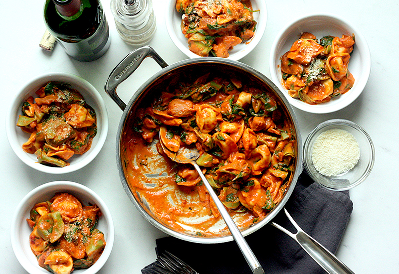 Spinach and tomato torellini in a pan and served in four bowls