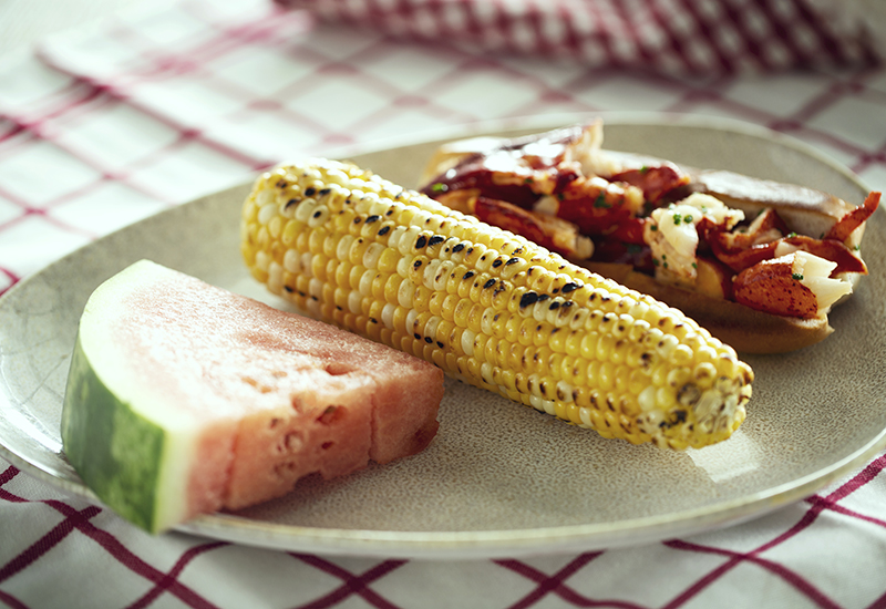 Lobster roll, corn, and watermelon on a plate