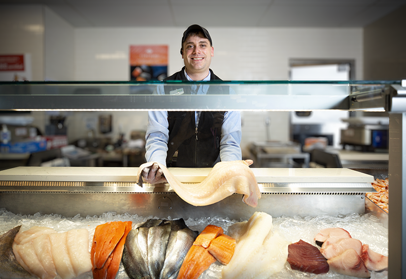 Heinen's Fishmonger Behind the Seafood Case Holding Raw Halibut Fillet