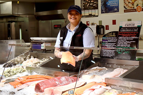 Heinen's fishmonger smiling while holding a fresh salmon fillet at a seafood counter with sustainable 