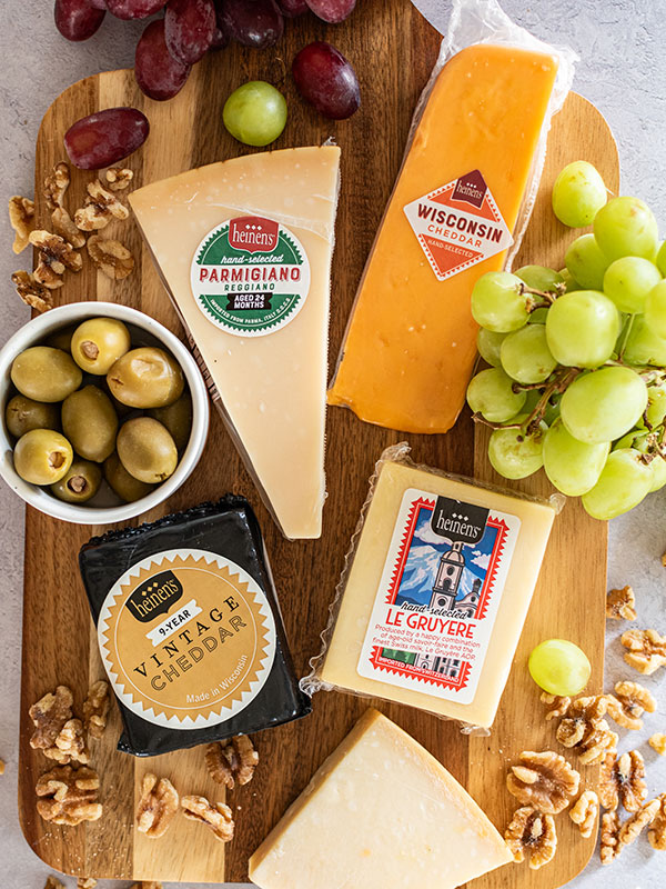 Heinen's Hand-Selected Cheeses on a Cheese Board with Grapes, a Bowl of Olives and Scattered Walnuts