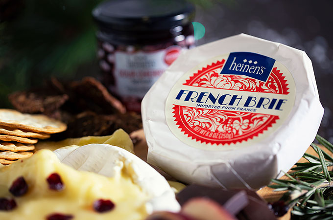 Heinen's Hand-Selected French Brie in it's Packaging with Fresh, Herbs, Crackers and a Jar of Fruit Preserves