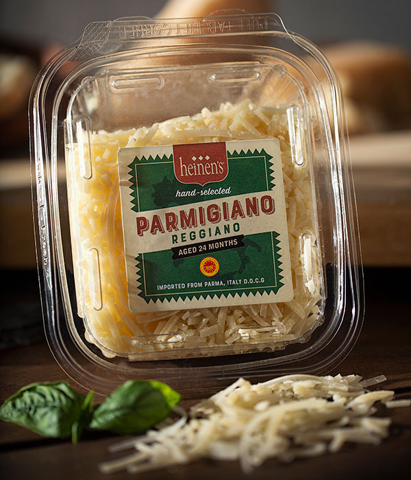 Heinen's Hand-Selected Parmigiano Reggiano in it's Packaging with Fresh Basil Leaves and Cheese Shreds