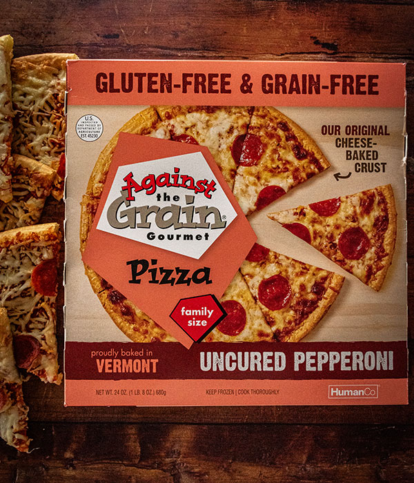 Against the Grain Frozen Pizza Box with Cooked Pizza Slices on a Wood Surface