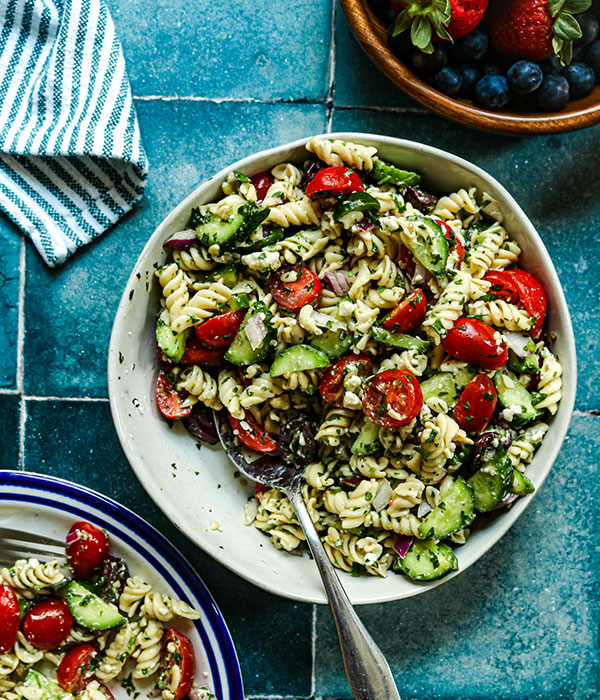 Better For You Greek Pasta Salad in a Serving Bowl with a Serving Spoon