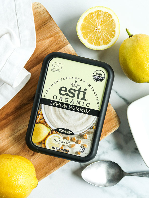 Esti Organic Lemon Hummus on a Wood Cutting Board with Fresh Sliced Lemons and a Spoon