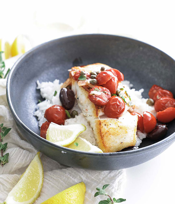 Mediterranean Halibut in a Bowl with Rice, Cherry Tomatoes, Olives and Lemon. Lemon Slices on the Side.