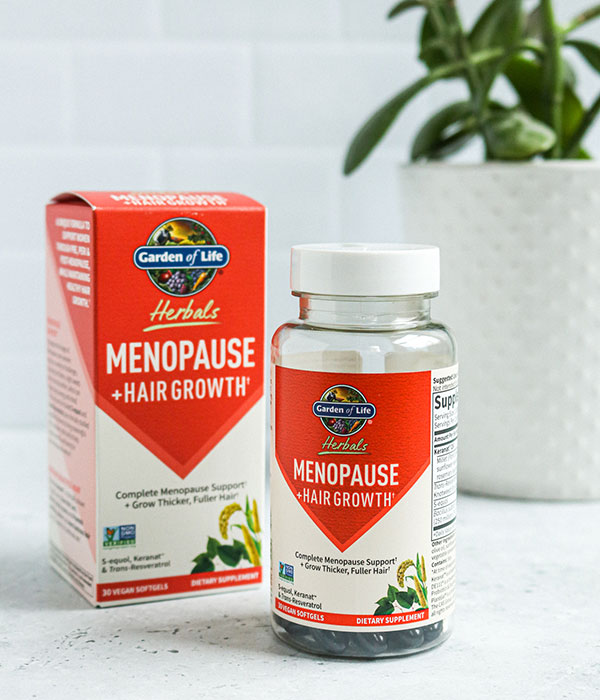Garden of Life Menopause Supplement Box and Bottle on a Slate Gray Surface with a subway tile background and a plant.