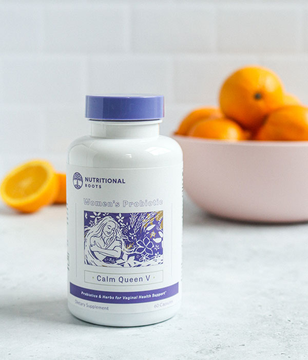 Nutritional Roots Probiotic Bottle on a on a Slate Gray Surface with a subway tile background and a bowl of oranges.