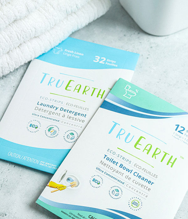 TrueEarth Laundry Detergent Sheets and Toilet Cleaner Sheets in their Packaging on a Slate Gray Surface with a Dish Towel