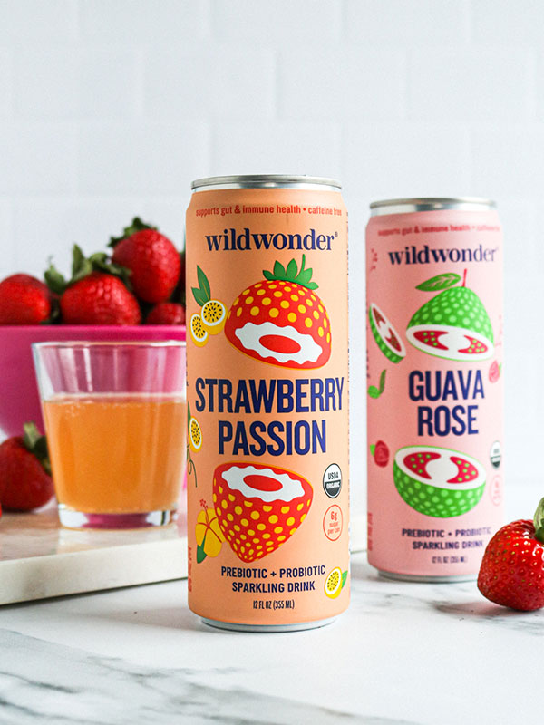 Wildwonder Strawberry Passion and Guava Rose Prebiotic and Probiotic Sparkling Beverages with a Bowl of Fresh Strawberries and a Filled Glass
