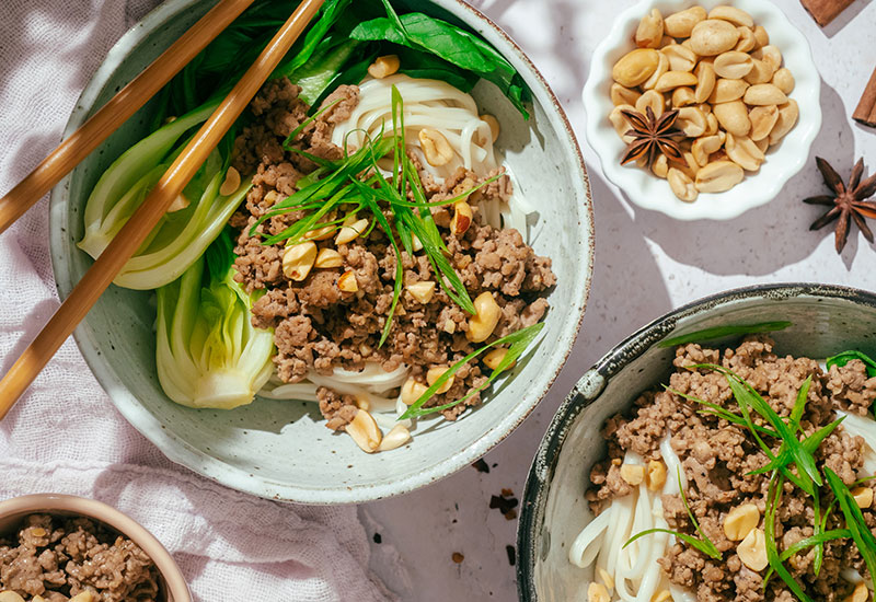 Up-close Photo of Easy Dan Dan Noodle Bowl with Bok Choy, Cooked Pork and a Bowl of Peanuts