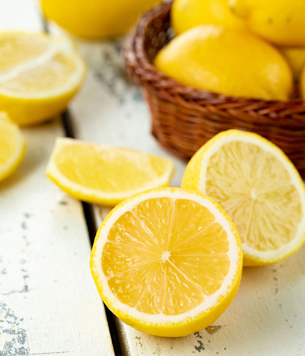 Fresh Lemon Slices on a Distressed White Wood Background with a Woven Basket Full of Lemons in the Background