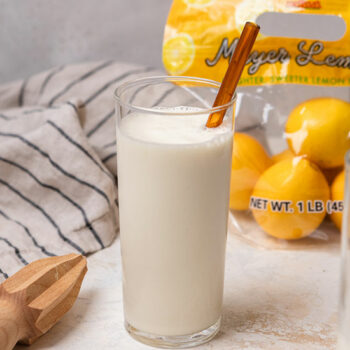 Copycat Frosted Lemonade in a Glass with a Straw, Dish Towel and a bag of Meyer Lemons in the Background.