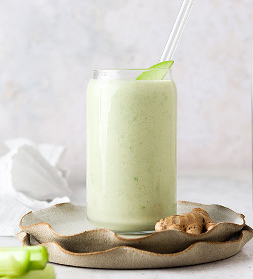 Apple Celery Smoothie in a Glass with a Glass Straw, Fresh Ginger and Fresh Celery