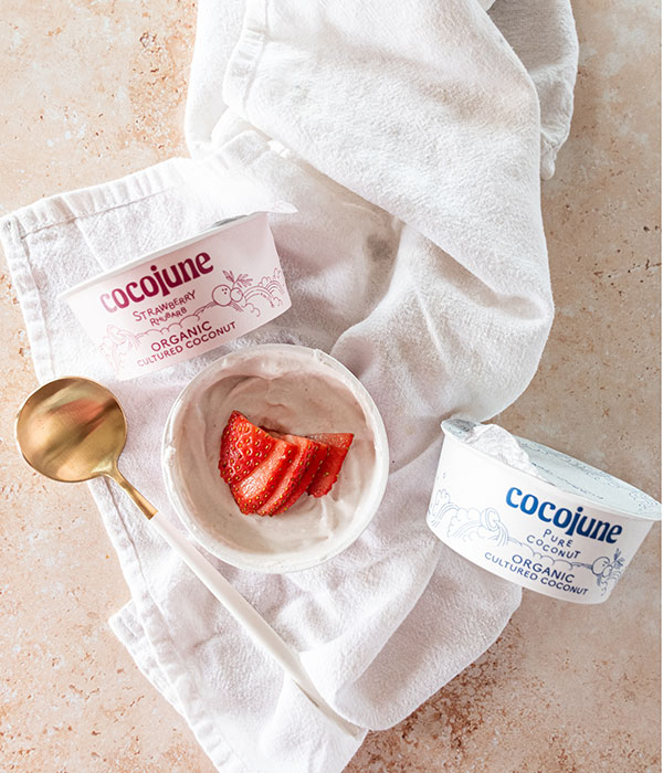 Cocojune Yogurt Cups on a White Dish Towel with a Spoon and Fresh Strawberries