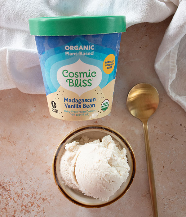 Cosmic Bliss Ice Cream Packaging on a Neutral Surface with a Bowl of Ice Cream and a Gold Spoon