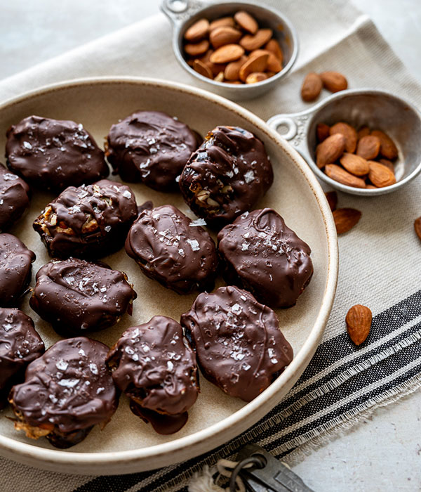 Mini Chocolate Covered Dates Snickers Bars on a Plate with Bowls of Almonds Beside