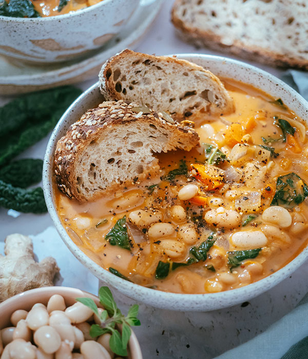 A Bowl of Ginger Coconut White Bean Soup with Two Sliced of Artisan Bread and a Bowl of White Beans Beside.