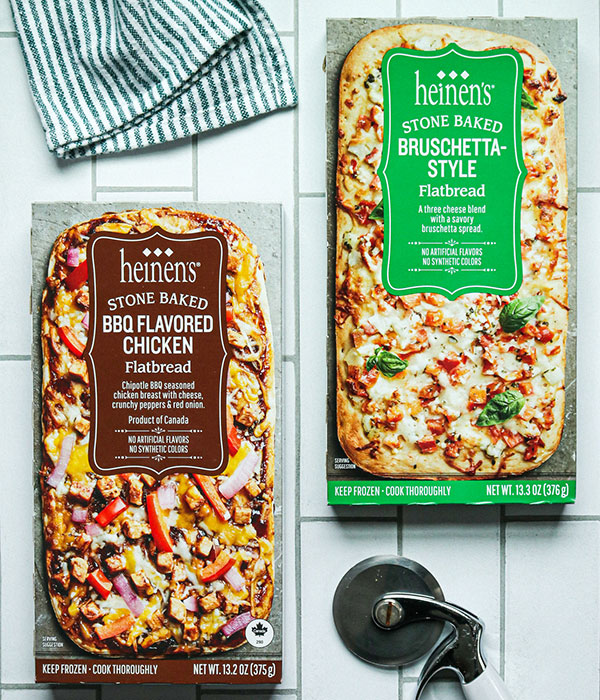 Heinen's Frozen Flatbreads in Packaging on a Tile Surface with a Pizza Cutter and Green Striped Dish Towel