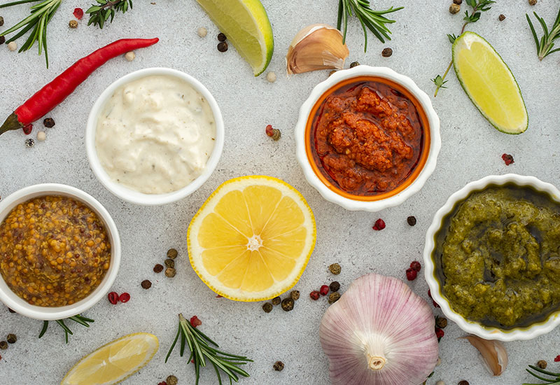 A Top Down Photo of International Sauces and Spices in Bowls with Fresh Produce and Herbs Surrounding